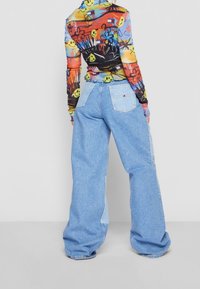 Colorful long-sleeve top featuring a graphic print, paired with high-waisted, wide-leg light blue denim jeans with back pockets.