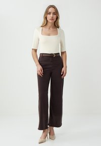Crème-kleurige bodysuit met vierkante halslijn, gecombineerd met bruine wijde broek en een bruine riem. Beige hakken maken de outfit compleet.