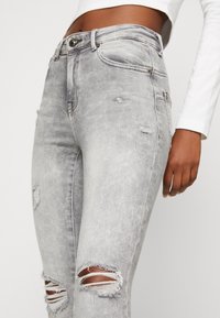 Šedé opotřebované džíny z denimu, s vysokým pasem, úzkým střihem a výraznými roztrženími na kolenou. Zpevněné švy.