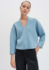 Lichtblauwe geribde trui met een V-hals en lange mouwen, gecombineerd met zwarte broek, met een ontspannen pasvorm en textuurstof.