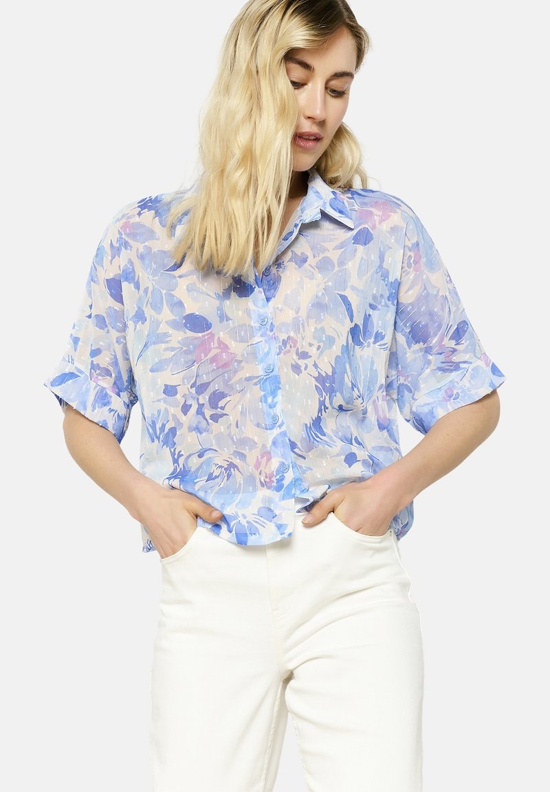 Lengvas, permatomas trumpomis rankovėmis marškinėliai šviesiai mėlynos spalvos su gėlių raštu mėlynos ir levandų atspalviais. Mygtukų užsegimas priekyje ir laisvas siluetas.