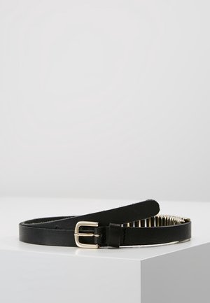 Czarny skórzany pasek ze złotą klamrą, zwinięty na białej powierzchni na jednolitym jasnoszarym tle.