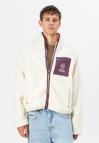 White, fluffy fleece jacket with a maroon chest pocket and zipper, featuring an embroidered design. The jacket has a high collar and zippered side pockets.