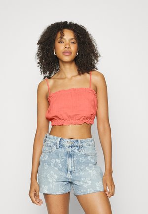Top cropped coral com bordas em babados e alças finas, combinado com calções de ganga claros com padrões florais e bainha desfiada.