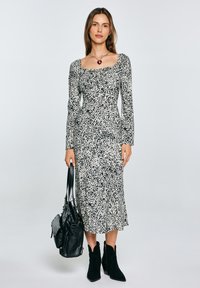 Abito stampato in bianco e nero con maniche lunghe e scollo quadrato, abbinato a stivali neri alla caviglia e a una borsa nera.