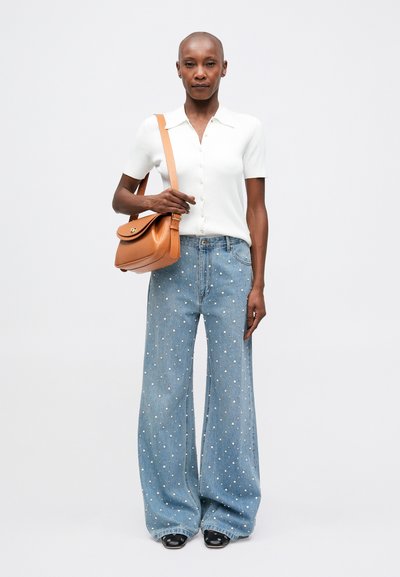 Witte geribde shirt met korte mouwen, lichtblauwe wijde jeans met zilveren versieringen en een bruine crossbody tas. Zwarte schoenen maken de look compleet.