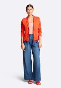 Roter Blazer, gestreifes Tanktop, hochgeschnittene weit geschnittene Jeanshose und rote Sandalen. Einfaches Design mit glattem Stoff und kontrastierenden Farben.