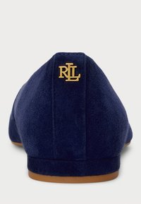 Sapatilha de camurça azul-marinho com bico arredondado, apresentando um logo dourado "RL" na parte de trás e uma sola lisa em tom de creme. Design simples e elegante.