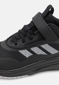 Schwarzer Sportschuh aus Mesh- und Synthetikmaterial. Verfügt über einen Klettverschluss, schwarze Schnürsenkel und weiße Streifenverzierungen an der Seite.