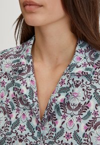 Overhemd met knopen in een bloemenpatroon in paars, roze en teal op een lichtblauwe achtergrond. Zachte stof met een notch-kraag en korte mouwen.