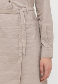 Abito in corduroy beige con cintura a cravatta, caratterizzato da una texture a righe verticali, dettagli con bottoni e maniche lunghe con estremità a polsino.