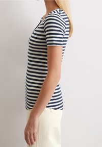 Stripet t-shirt i marineblå og creme, korte ærmer, rund halsudskæring, tætsiddende design, blødt bomuldsstof, synlige sømme langs kanten.