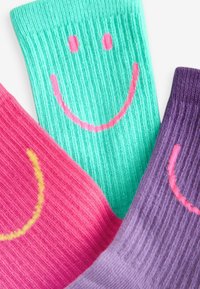 Bunte gerippte Socken in Pink, Grün und Lila mit lächelnden Gesichtsmotiven in kontrastierenden Fäden. Weicher Stoff und verspielte Muster.