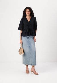 Črn peplum top z kratkimi, razširjenimi rokavi, detajli iz očesa in sprednjim vezanjem. Kombiniran z svetlo modro denim maxi krilo in bež torbico.