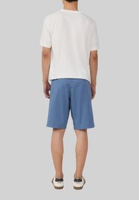 Witte katoenen t-shirt met korte mouwen, gecombineerd met blauwe katoenen shorts en witte sneakers met zwarte accenten. Uitzicht van achteren.