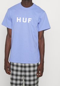 Světle modré bavlněné tričko s krátkými rukávy a bílým potiskem "HUF" na přední straně, spárováno s černo-bílými kostkovanými šortkami.