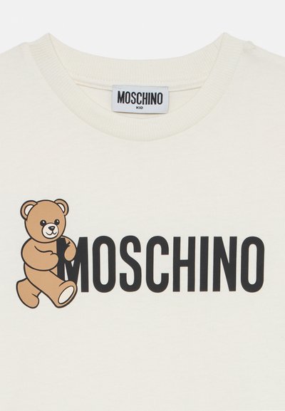 Bílý bavlněný tričko s kresleným hnědým medvědem a výrazným černým nápisem "MOSCHINO". Design s žebrovaným kulatým výstřihem, hladká textura.