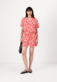 Floral two-piece outfit featuring a cropped, short-sleeve top and matching shorts in bright coral with white flowers. Smooth fabric, casual fit.