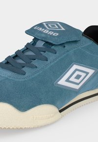 Μπλε καστόρινο αθλητικό παπούτσι Umbro με λευκό διπλό διαμαντένιο λογότυπο στο πλάι και στη γλώσσα, υφασμένα κορδόνια και εκρού σόλα με μαύρη ρίγα.