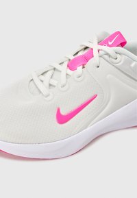 Light gray athletic shoe with a textured upper, pink accents on the tongue and swoosh logo, and a white outsole. Lace-up design.