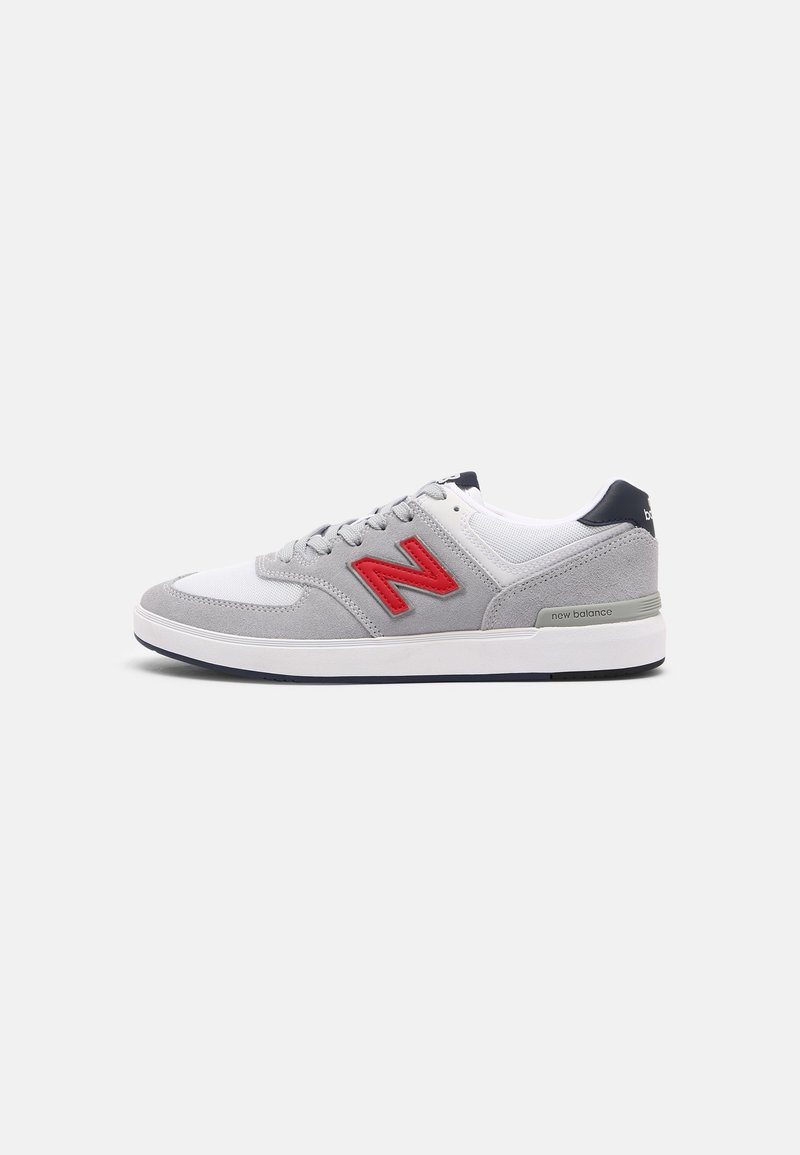 Šedé a bílé tenisky New Balance s červeným logem, šněrovací design a bílá podrážka, zobrazené z boku na jednoduchém pozadí.