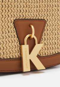 Vävd beige väska med bruna läderdetaljer och en gyllene metall "K"-berlock med inristat "Karl Lagerfeld" hängande från en läderögla.