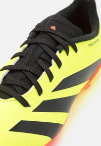 Scarpa da calcio gialla brillante con accenti neri, caratterizzata da una superficie texture, lacci neri e un design a strisce distintive. Suola in gomma visibile.