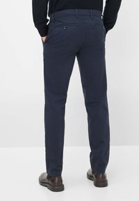 Pantalons bleu marine avec une coupe droite, fabriqués en tissu lisse. Comprend deux poches arrière avec des boutons et est associé à des chaussures noires.