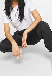 Svarta, lätta joggers med elastiska muddar, som pares med en åtsittande vit t-shirt och vita sneakers, i en avslappnad pose. Detaljer om avslappnad outfit.