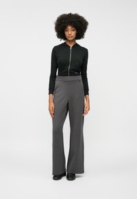 Μαύρη φούτερ ζακέτα με φερμουάρ και μπροστινή τσέπη, σε συνδυασμό με γκρίζες παντελόνες φαρδιάς γραμμής. Λείο ύφασμα, ελάχιστες λεπτομέρειες και ρουχισμός με κομψή σιλουέτα.