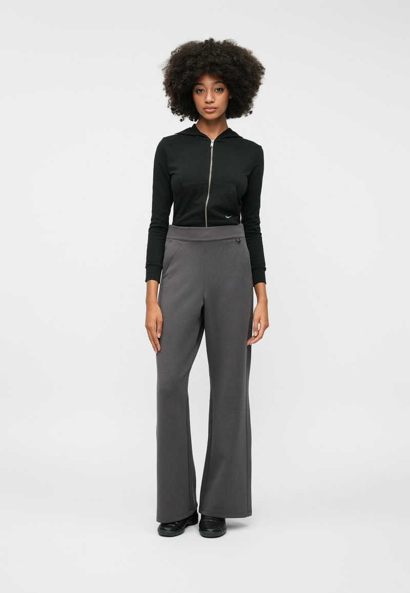Hoodie zippé noir avec une poche avant, associé à un pantalon large gris. Tissu lisse, accents minimalistes et silhouette épurée.