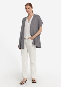 Lätt grå strukturerad kappa sjal över en vit skjorta och vita byxor, i kombination med svarta klacksandaler.