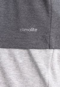 Šedá látka s nápisem "climalite" tištěným na tmavě šedém oděvu vrstveném na světlejší šedé látce pod ním.