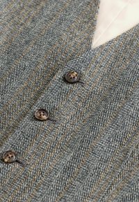 Houndstooth-patterned fabric in shades of gray and tan, featuring three dark buttons and a crisp, contrasting collar.