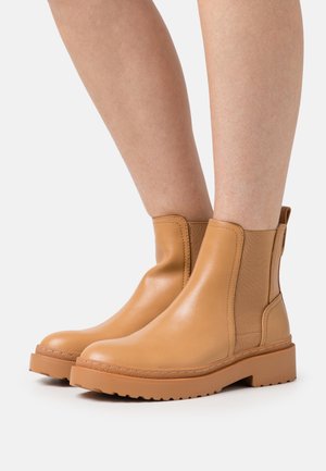 Bottes cheville en cuir tanné couleur sable, dotées de panneaux latéraux élastiques et d'une semelle en caoutchouc épaisse à finition texturée. Tige lisse avec des détails de coutures minimales.