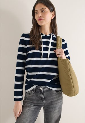 Sweat à capuche à rayures bleu marine et blanc avec manches longues, associé à un jean gris et un sac à bandoulière beige. Texture de tissu lisse et douce.