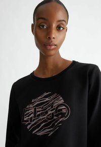 Felpa nera con un design grafico rotondo caratterizzato da linee rosa e argento e testo. Tessuto morbido con scollatura a girocollo e maniche lunghe.