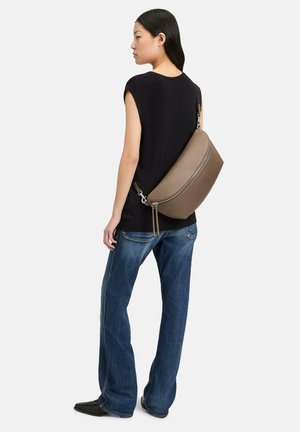 Braune Leder-Umhängetasche mit einer geschwungenen Form, silberner Hardware und einem Reißverschluss, getragen über einem schwarzen Oberteil und blauen Jeans.