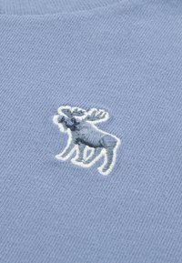 Lys blå strikket stof med et broderet elgdesign i nuancer af blå, omridset i hvidt, centreret på tøjet.