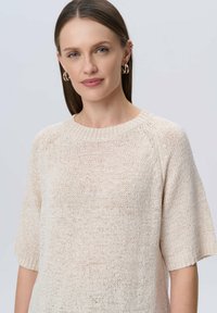 Jasnobeżowy sweter dzianinowy z okrągłym dekoltem i krótkimi rękawami, o luźnym, teksturowanym wzorze. Miękka tkanina z luźnym krojem.