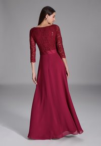 Lång burgundykjol med en spetslivstycke och trekvartslånga ärmar samt en svävande satängkjol. Designen har en figursydd midja.