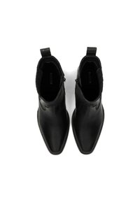 Botas de cuero negro hasta el tobillo con punta afilada, costuras decorativas en los laterales y un lazo en la parte trasera. Textura suave, detalles mínimos.