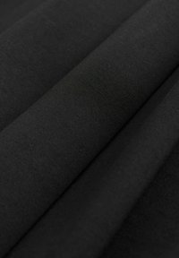 Gros plan sur un tissu noir plié avec une texture lisse, finement tissée et de légères marques de plis diagonales.