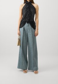 Top negro sin mangas con detalles de volantes combinado con pantalones de mezclilla azules de pierna ancha. Accesorios con un pequeño bolso beige y sandalias beige.