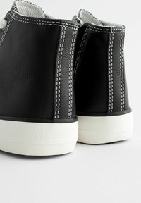 Schwarze Knöchelstiefel mit einem strukturierten Lederobermaterial, weißen Gummisohlen und kontrastierenden weißen Nähten entlang der Nähte.