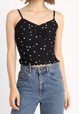 Černý žebrovaný top na ramínka s barevnými puntíky, nastavitelné tenké ramínka a volánkový lem. Kombinován s modrými džíny s vysokým pasem.