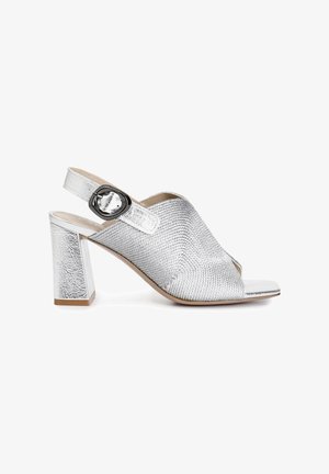Sølvfarvet mønstret hæl sandal med åben tå, slingback design og en rund spænde detalje på stropperne. Struktureret metallisk finish.