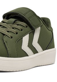 Grön sneakers med en texturerad ovandel, nylon snörning och ett kardborreband. Har krämfärgade ränder och en vit gummisula.