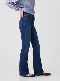 Flared blue denim jeans with a mid-rise fit, five-pocket design, and subtle stitching details; paired with black ballerina flats.
