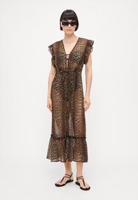 Vestido maxi transparente con estampado de leopardo, mangas con volantes, cintura ajustada y dobladillo en capas; sandalias negras completan el conjunto.